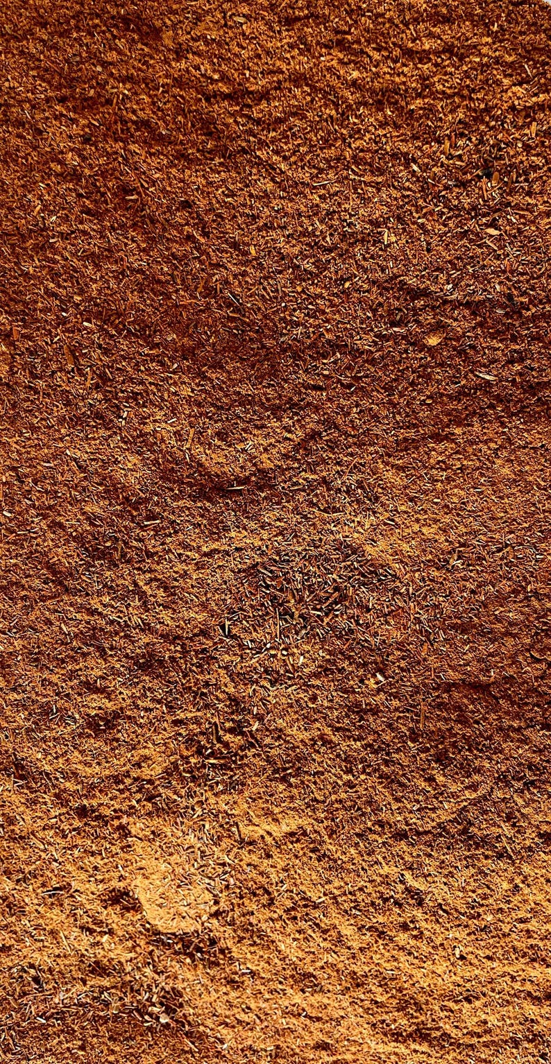 May include: Close-up of a pile of ground cinnamon, a warm brown spice with a slightly reddish hue. The cinnamon is finely ground and has a slightly rough texture.