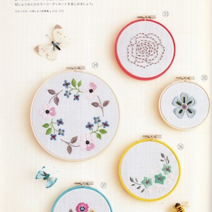 May include: Five embroidery hoops with different floral designs. The hoops are in various colors, including red, blue, yellow, and turquoise. The designs include a rose, a wreath of flowers, a single flower, a cluster of flowers, and a vine with leaves and flowers. The hoops are all 10 cm in diameter.