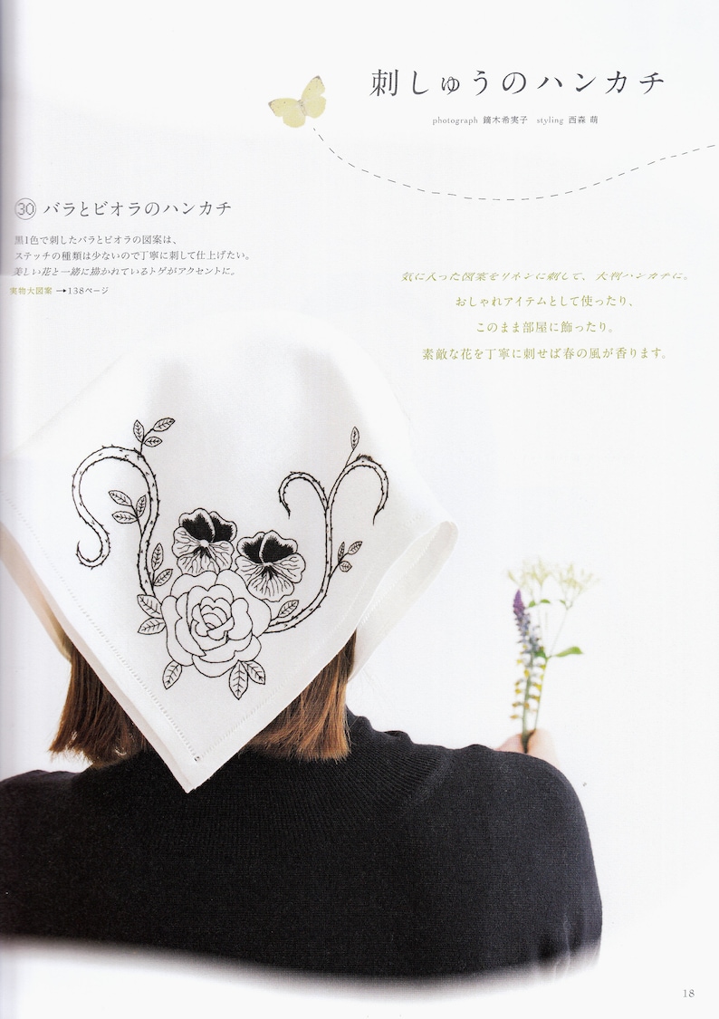 May include: A white handkerchief with black embroidery of a rose and two pansies. The handkerchief is folded and draped over the shoulder of a person wearing a black turtleneck sweater.
