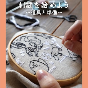 Puede incluir: Primer plano de una persona bordando una tela blanca con hilo blanco y negro en un aro de bordado de madera. La tela presenta un diseño de animales y plantas. El texto "1 章 刺繍を始めよう～道具と準備～" es visible en la imagen.