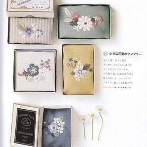 May include: Five small embroidered fabric squares in different colors, each with a floral design. The squares are displayed in a white box with a white background. The text "Lithographie AZ&Eacute;MARD COUSINS NIMES" is on the top of the box. The text "VERITABLE FIL CB ALA CROIX CARTIER-BRESSON PARIS ART 19" is on the left side of the box. The text "15 小さな花束のサンプラー 大きな花、小さな花を それぞれバランスよく束ねた ブーケのサンプラーです。 土台布の色との組み合わせも 楽しみながら、ハンカチや ブラウスに刺しても素敵です。 刺しゅう図案集p.103" is on the right side of the box.
