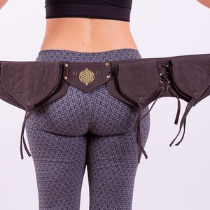 Puede incluir: Un cinturón de cuero marrón con múltiples bolsillos y una hebilla de metal decorativa. El cinturón tiene un patrón geométrico y está atado con cordones.