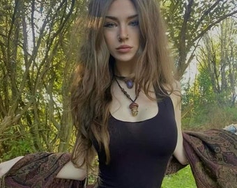 May include: A woman with long brown hair wearing a black tank top, a brown leather belt with a pouch, and a purple and brown patterned scarf. She is wearing a necklace with a purple stone and a mushroom pendant.