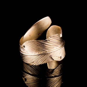 Peut inclure: Une bague dorée avec un motif de plume. La bague est réglable et peut être portée à n'importe quel doigt.