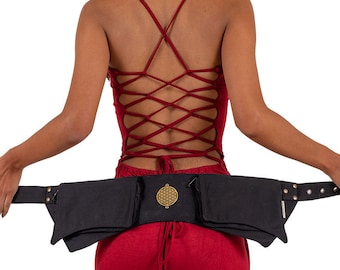 May include: A black canvas belt with multiple pockets and a gold metal buckle featuring a geometric design. The belt is worn around the waist of a person wearing a red top.