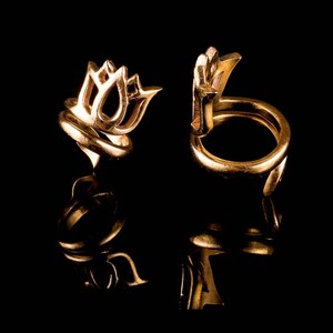 May include: Two gold rings with a flower design. The rings are on a black background.