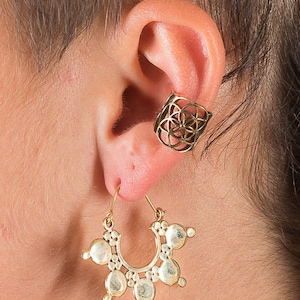 May include: Gold ear cuff with a geometric design and a gold hoop earring with a circular design.