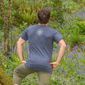 K&ouml;nnte beinhalten: Eine Person tr&auml;gt ein dunkelblaues T-Shirt mit einem wei&szlig;en geometrischen Muster auf dem R&uuml;cken. Die Person steht auf einem Feld mit lila Blumen.