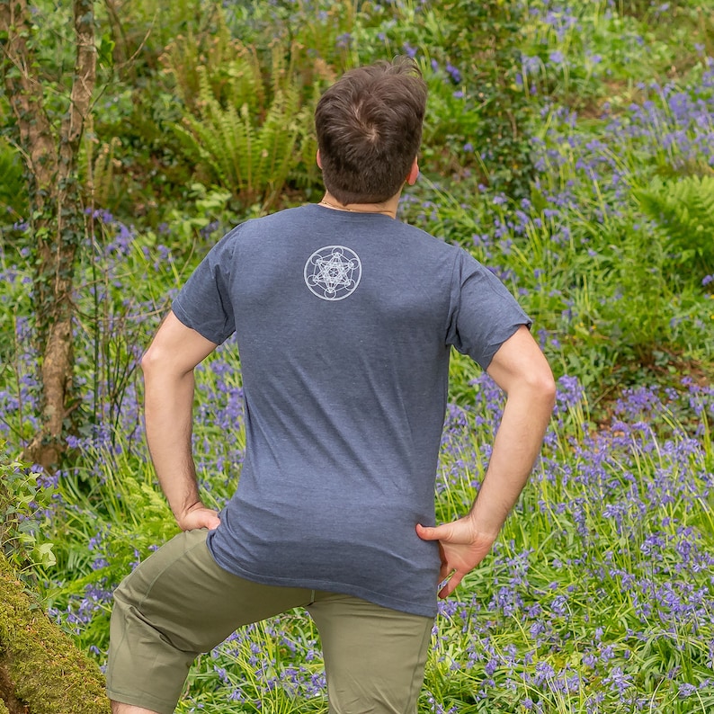K&ouml;nnte beinhalten: Eine Person tr&auml;gt ein dunkelblaues T-Shirt mit einem wei&szlig;en geometrischen Muster auf dem R&uuml;cken. Die Person steht auf einem Feld mit lila Blumen.