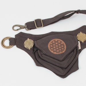 May include: A brown canvas fanny pack with a zippered pocket and a flower of life design. The pack has a strap with a metal clip and a metal ring.