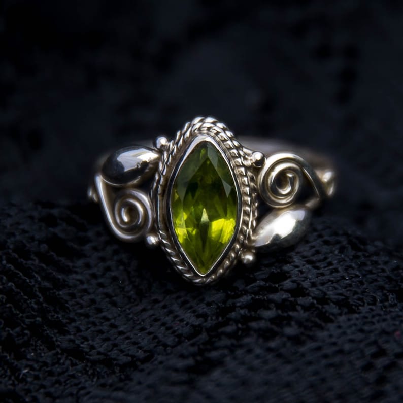 May include: A silver ring with an ornate design features a marquise-shaped green gemstone.