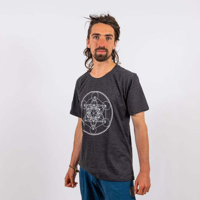 K&ouml;nnte beinhalten: Ein dunkelgraues T-Shirt mit einem wei&szlig;en geometrischen Design auf der Vorderseite. Das Design ist ein komplexes Muster aus Kreisen und Linien.