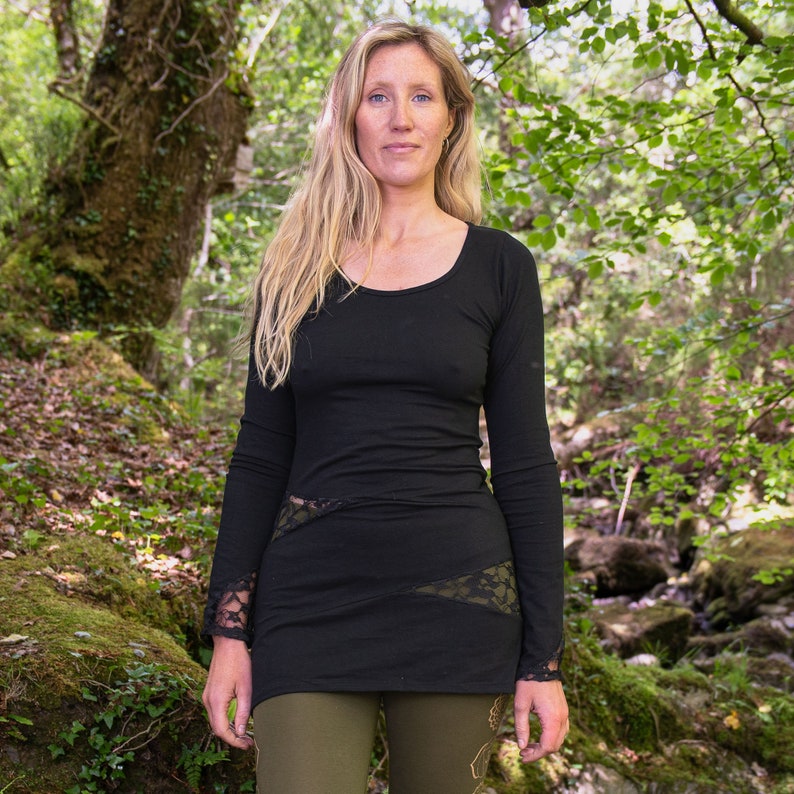 May include: A black long-sleeved shirt with lace detailing on the sleeves and sides. The shirt is worn by a person standing in a forest setting.