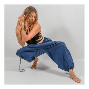 Puede incluir: Una mujer con un top negro corto y pantalones azules anchos con cintura de cord&oacute;n. Est&aacute; en una postura de yoga con los brazos cruzados frente a ella.