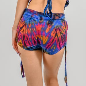 May include: Tie-dye shorts with a blue, pink, orange, and black color scheme. The shorts have a drawstring waist and side ties.