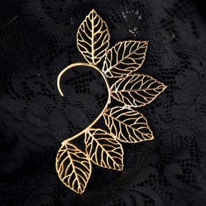 May include: Gold leaf ear cuff with a delicate, intricate design. The cuff is made of thin metal and features multiple leaves that are connected to form a curved shape.