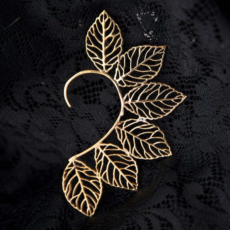 May include: Gold leaf ear cuff with a delicate, intricate design. The cuff is made of thin metal and features multiple leaves that are connected to form a curved shape.