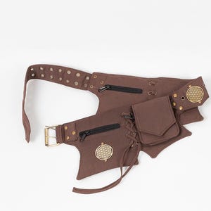 May include: Brown waist belt with multiple pockets, zippers, and decorative metal accents. The belt features a buckle closure and a series of eyelets for adjustment. A small pouch is attached with a decorative lace-up detail. The belt has a unique, asymmetrical design.