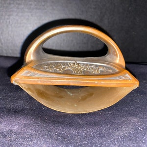 May include: Antique bronze-colored iron with a curved handle and a decorative floral design on the top. The iron has a rounded base and a handle for easy grip. The overall design is ornate and vintage.