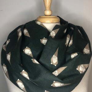 May include: A dark green infinity scarf with a repeating pattern of brown gnomes. The gnomes have white faces and white hats.