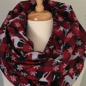 May include: Red and black plaid infinity scarf with a white snowflake and reindeer pattern.