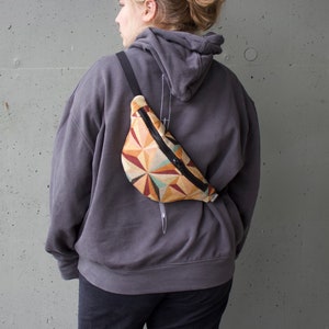 May include: A person wearing a gray hoodie with a black fanny pack with a geometric pattern in shades of brown, orange, and beige.