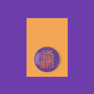 Può includere: Un bottone viola con il testo tedesco "ICH MUSS GAR NICHTS!" in lettere arancioni. Il bottone è posto su un rettangolo arancione su sfondo viola.