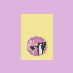 May include: A humorous illustration of a black and white cat on a pink button, holding a phone. The button is on a yellow rectangle, set against a purple background. The text on the button reads "STOP CATCALLING!"