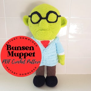 May include: A crochet pattern for a green Bunsen Honeydew Muppet. The pattern is available as an instant download. The image shows a completed crochet doll wearing a blue jacket, a red tie, and black glasses.