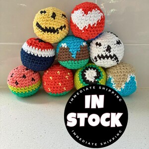 May include: A collection of colorful, crocheted balls with various designs, including a smiley face, a heart, a skull, a watermelon, and a strawberry. The balls are in a variety of colors, including red, yellow, blue, green, and white.