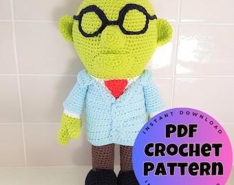 May include: A handmade, lime green crochet doll wearing black glasses, a light blue jacket, and a red tie. The doll has brown legs and black shoes. A circular graphic reads "PDF CROCHET PATTERN".