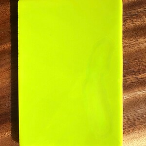 May include: A rectangular, neon green object with rounded corners. The object is set against a wooden surface. The bright green color is the dominant feature, creating a vibrant and eye-catching appearance.