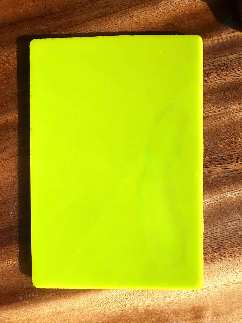 May include: A rectangular, neon green object with rounded corners. The object is set against a wooden surface. The bright green color is the dominant feature, creating a vibrant and eye-catching appearance.
