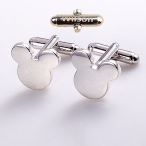 May include: Silver cufflinks with a Mickey Mouse head design. The cufflinks come with a gold-toned gift box engraved with the name "Wilson".