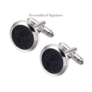 Puede incluir: Un par de gemelos de plata con un diseño redondo negro y brillante. Los gemelos tienen un acabado liso y pulido.