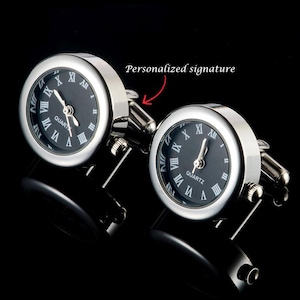 May include: A pair of silver cufflinks with black clock faces. The clocks have Roman numeral hour markers and the words "QUARTZ" printed on them.