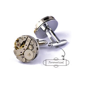 May include: Silver cufflinks featuring a mechanical watch movement design. The cufflinks showcase intricate gears and springs, with the word "Personalized" in a drawing. A unique accessory.