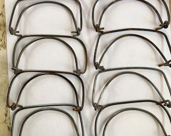 May include: A collection of twelve semi-circular metal handles arranged in two vertical columns. Each handle features a curved wire frame with small, integrated loops at the ends for attachment, showing a weathered, dark grey metallic finish.