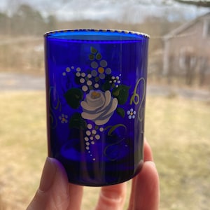 May include: A cobalt blue glass shot glass with a white, blue, and green floral design painted on the side.
