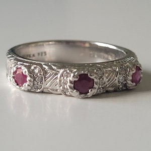 May include: A silver band ring with three red gemstones and small white gemstones set in the band.