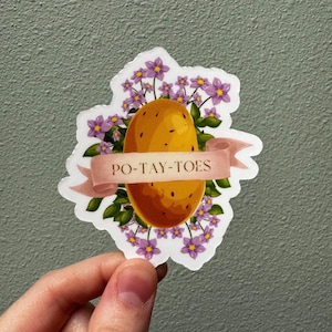 May include: A white sticker with a cartoon illustration of a potato surrounded by purple flowers. The text "PO-TAY-TOES" is written on a pink banner.