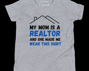 May include: Gray t-shirt with a black house graphic and blue text that reads "My Mom is a Realtor and she made me wear this shirt."
