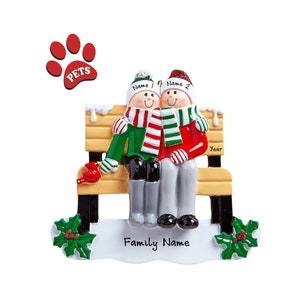 May include: A Christmas ornament featuring two figures sitting on a park bench. The figures are wearing winter hats, scarves, and boots. The bench is yellow with black legs. The ornament has a paw print with the word "PETS" and a sign that says "Family Name".