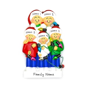 May include: A Christmas ornament featuring a family of five holding Christmas lights. The ornament is white with red, blue, and green accents. The family is smiling and has names written on their hats. The ornament says "Family Name" at the bottom.