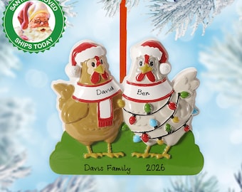 May include: A Christmas ornament featuring two chicken figures wearing Santa hats and scarves. One chicken is brown, the other is white and decorated with Christmas lights. The ornament is on a green base with the text "Davis Family 2026".