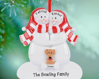 May include: A white Christmas ornament featuring two snowmen wearing red and white striped hats and scarves. The names Patrick and Rachel are written on the hats. A small brown dog sits below with the name Chase, and The Bowling Family is printed below.