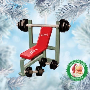 May include: A green weight bench Christmas ornament with red padding, black weights, and a silver barbell. The bench has the year "2024" and the name "Bart" written on it. A green circle with the words "Santa Approved" and "Ships Today" is in the background.