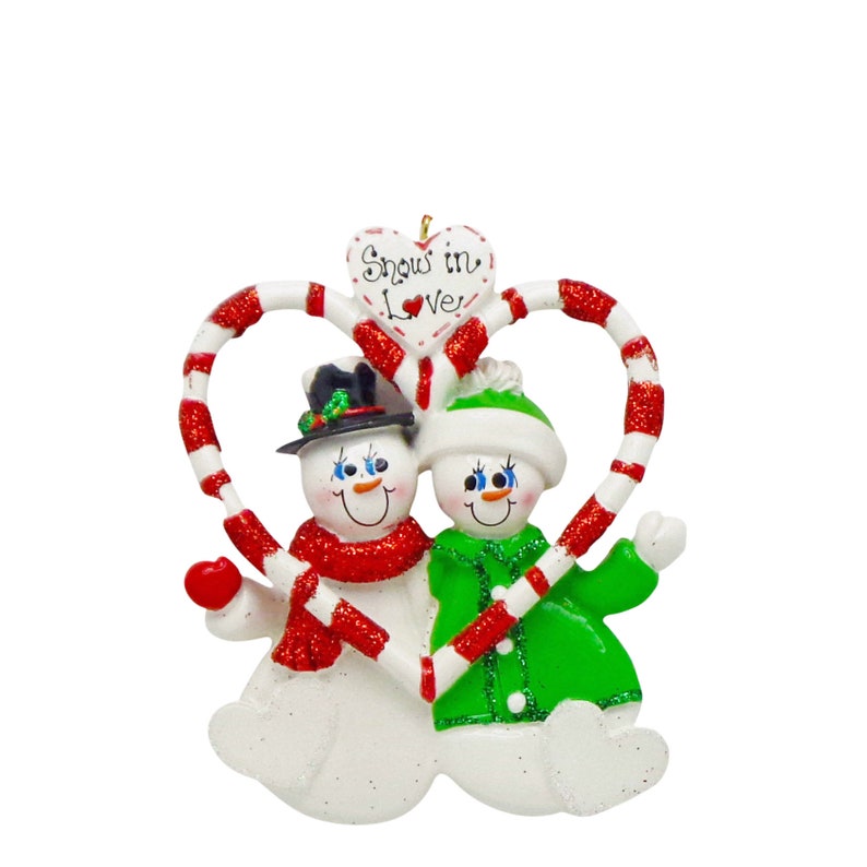 May include: A Christmas ornament featuring two snowmen holding candy canes that form a heart shape. The snowmen are wearing hats and scarves. The ornament has the text "Snow in Love" on a heart-shaped sign.