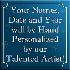 May include: A blue square sign with white snowflakes and white text that reads "Your Names, Date and Year will be Hand Personalized by our Talented Artist!"