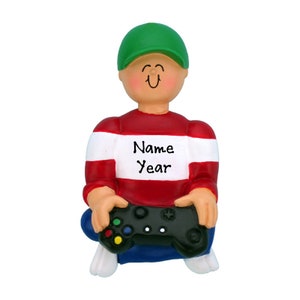 May include: A red and white striped sweater with the words "Name Year" on the front. The person is wearing a green hat and blue jeans and holding a black video game controller.